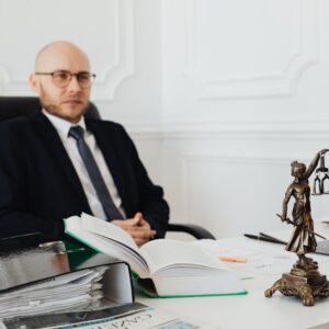 Bald lawyer in office sitting with legal documents and Justice statue. - Photo by www.kaboompics.com on Pexels