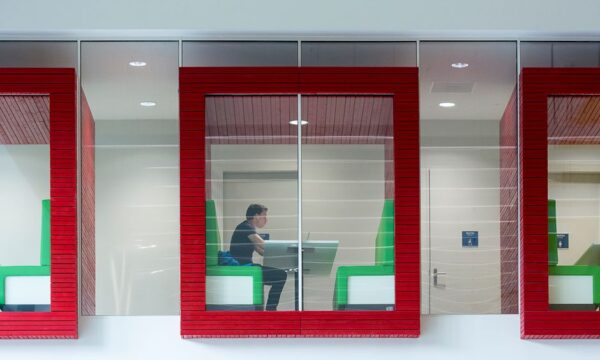 Contemporary coworking space with colorful booths and glass walls featuring a focused professional. - Photo by Jan van der Wolf on Pexels
